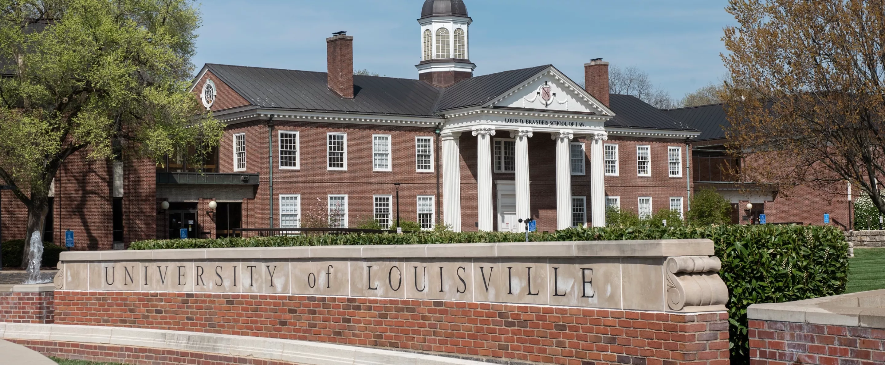 Louis D. Brandeis School of Law building in the background with the main University of Louisville entrance sign on 3rd Street.
